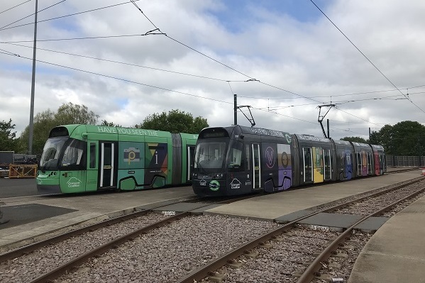 Photo of two trams next to each other, one wrapped in the original A-Z of Consent, with the other wrapped in the new Night-TIme A-Z of Consent
