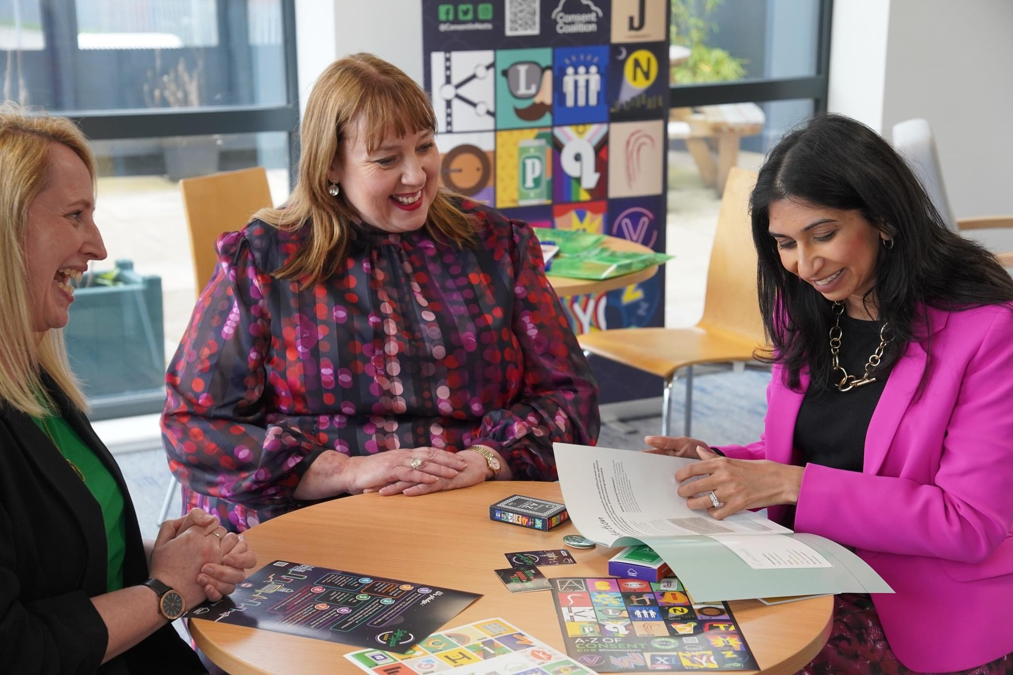 Photo of Louise (Consent Coalition Manager) sat around a table with Police and Crime Commissioner Caroline Henry and Home Secretary Suella Braverman, who is looking through the 'Your Journey' Booklet. Other coalition resources are on the table. Everyone is smiling.