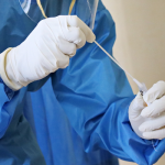 Picture of a forensic medical examiner, dressed in blue overalls, wearing white gloves, putting a swab into a test tube