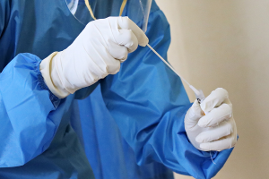 Picture of a forensic medical examiner, dressed in blue overalls, wearing white gloves, putting a swab into a test tube