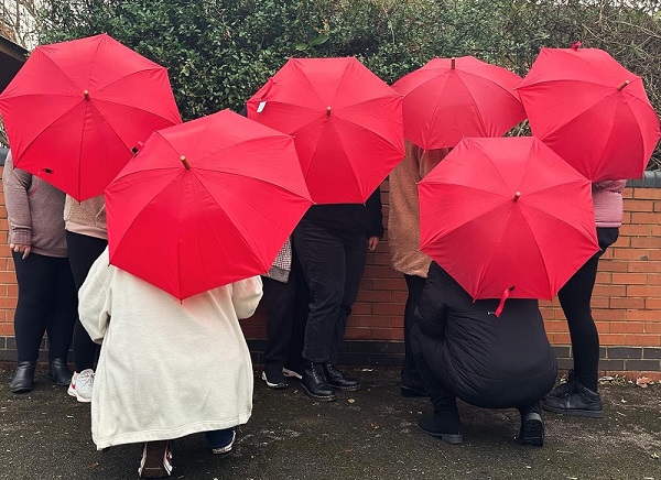 A group of people, facing away from the camera, with their red umbrellas up.