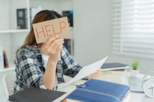 Woman sat at a desk, working, with on hand holding up a sign that says 'Help'
